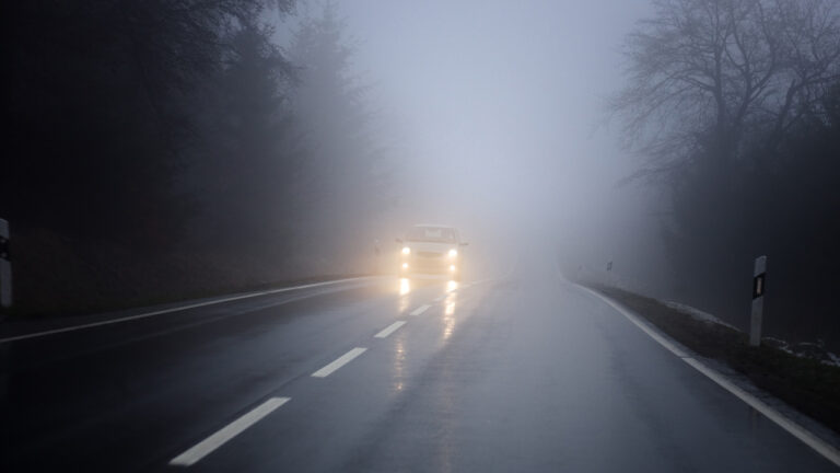 Vista di un auto con i fari accesi su una strada nella nebbia