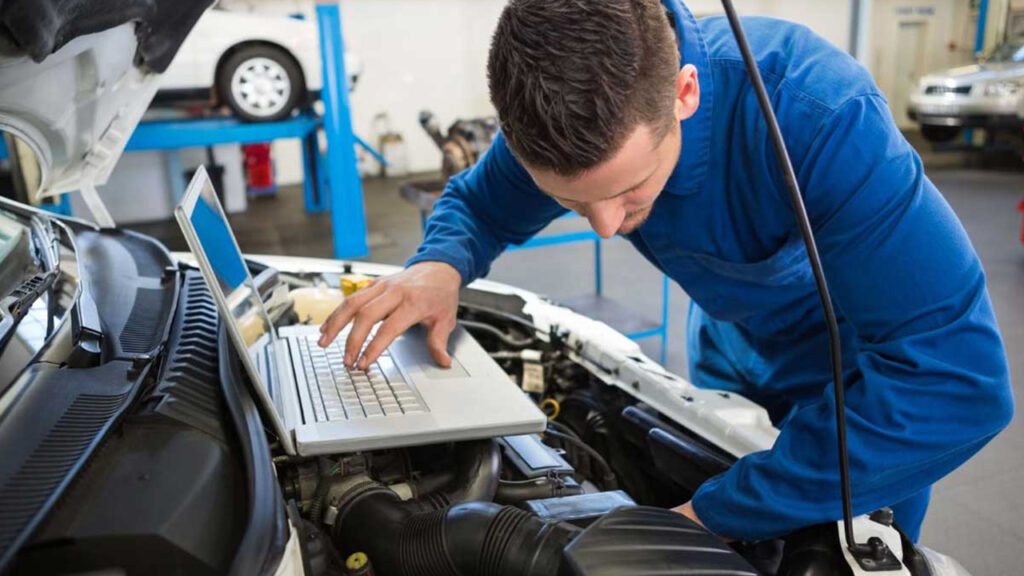 Immagine di un meccanico che lavora con un computer nel cofano anteriore di un auto